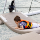 Child wearing a life jacket relaxing on the front deck netting of a family yacht charter